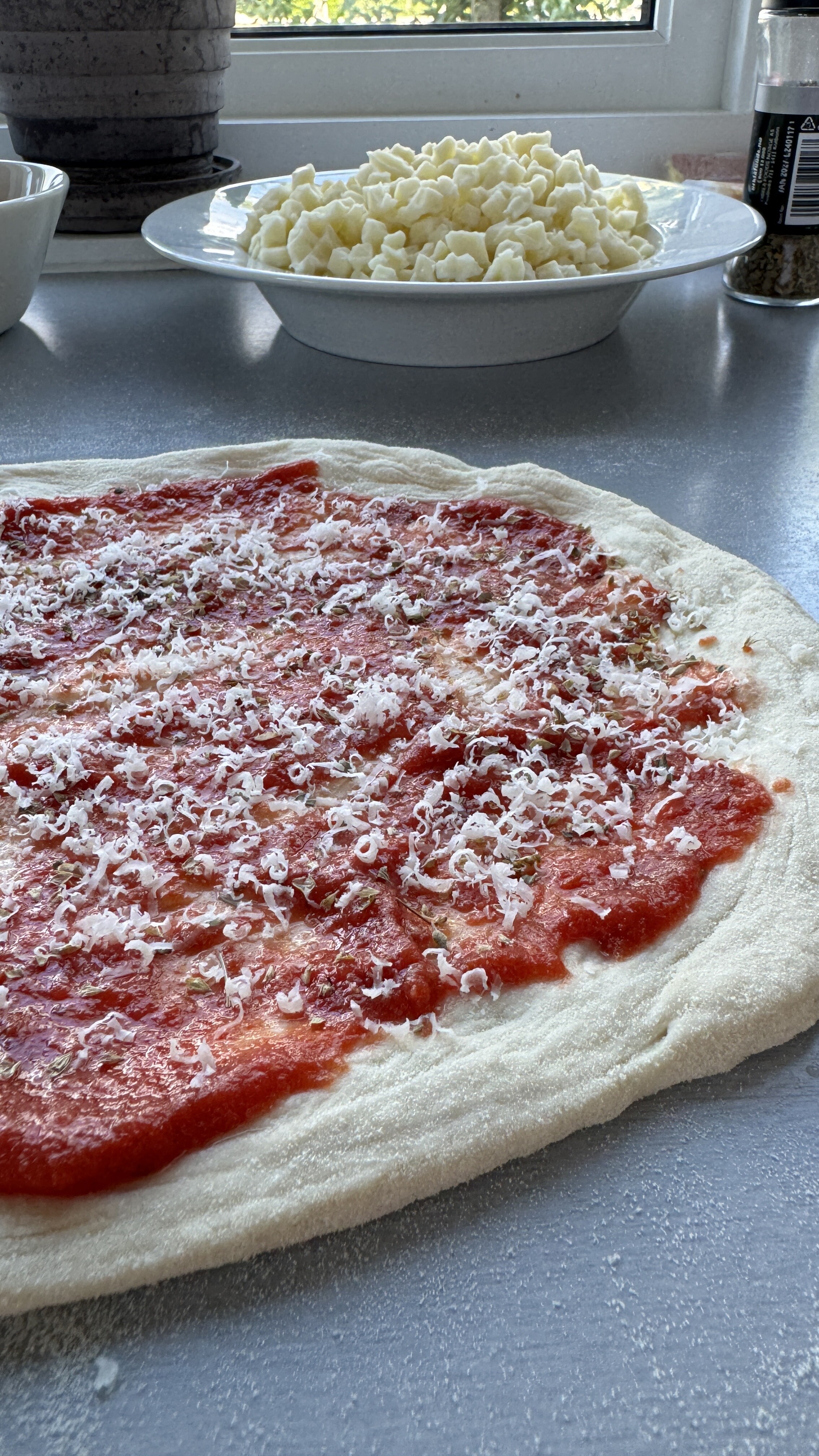 Utbakt pizzabunn med tomatsaus og parmeggiano på, cubetti i skål i bakgrunnen
